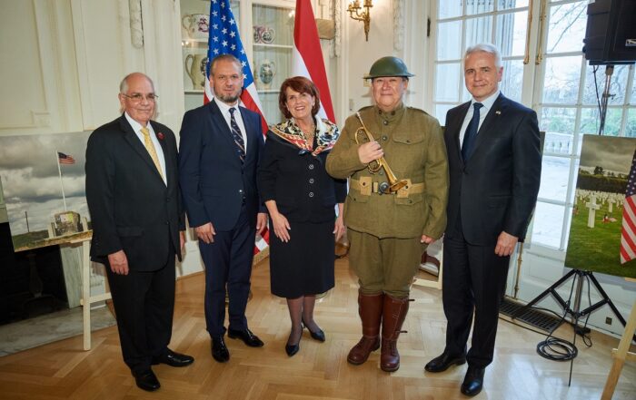 5 people, including a WWI interpreter, stand in a building in front of two flags