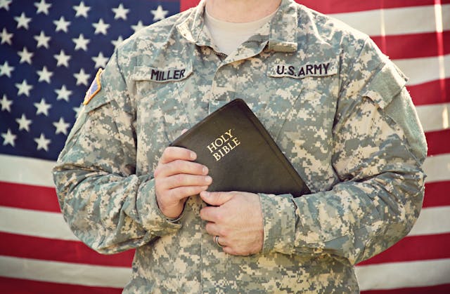 A soldier holding the Bible and standing in front of a U.S.A. flag