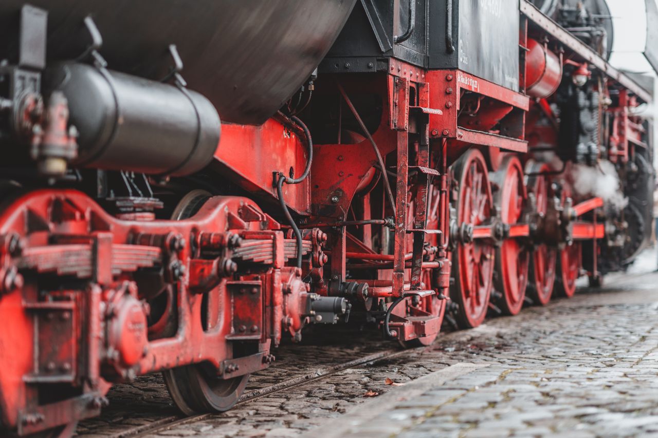 A close-up of red and black cast-iron drive wheels and mechanical linkage on a vintage steam locomotive, representing the industrial engineering that powered New Jersey's wartime rail network