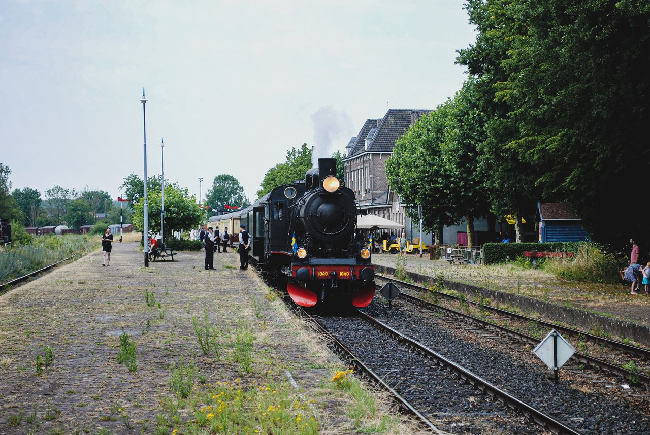 Alt text: A vintage black steam locomotive numbered 1040 arriving at a small rural station platform, with passengers and station staff standing nearby.