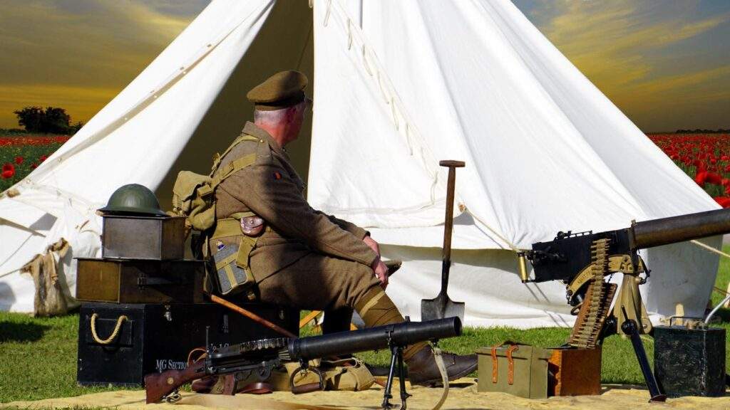 A man dressed as a WWI soldier sits by a tent with military gear in a field